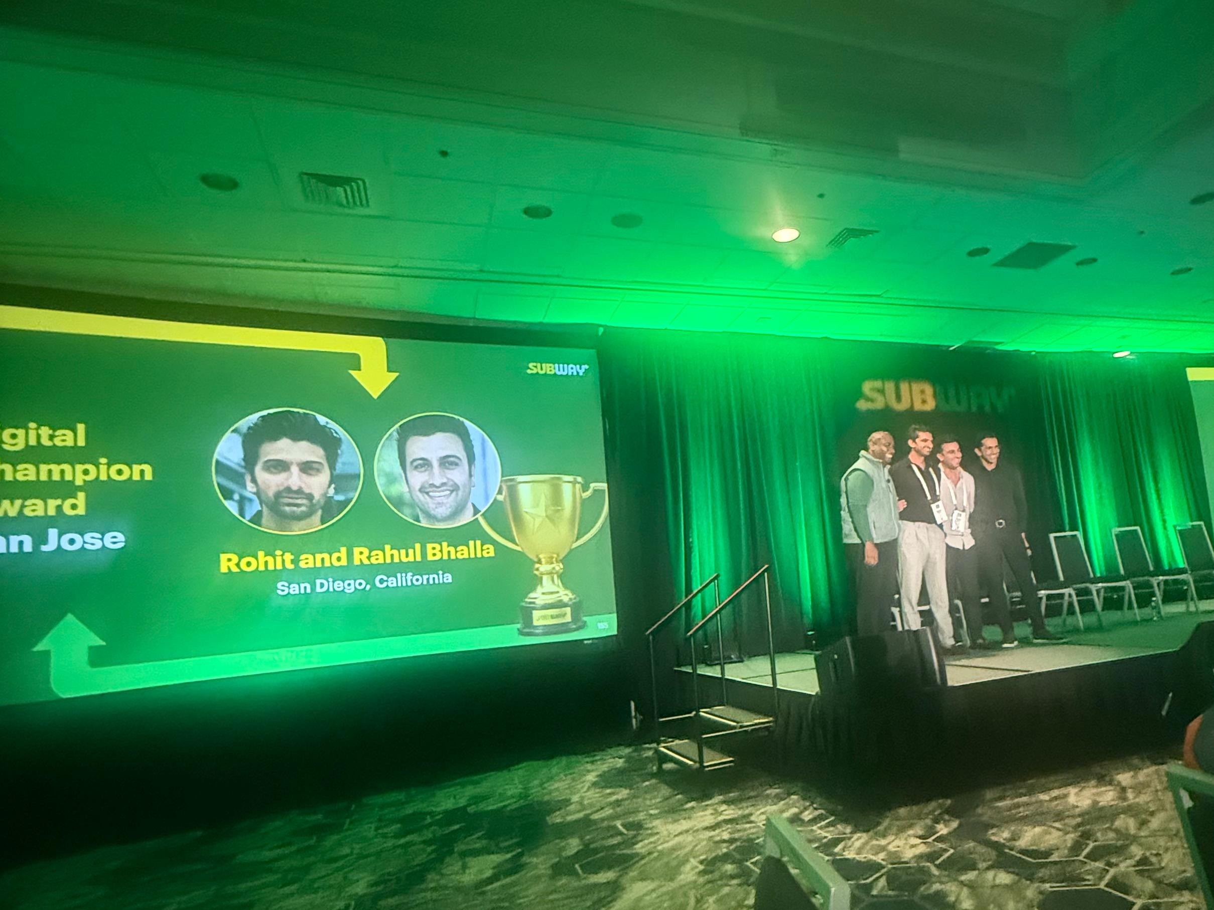 A Subway conference stage: the screen reads Digital Champion Award, San Jose, with photos of Rohit and Rahul Bhalla of San Diego, California beside a gold trophy